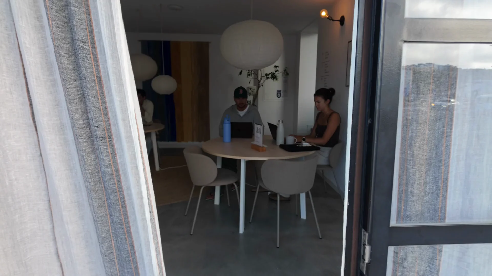 Guests working on laptops around shared tables in a bright coworking space.